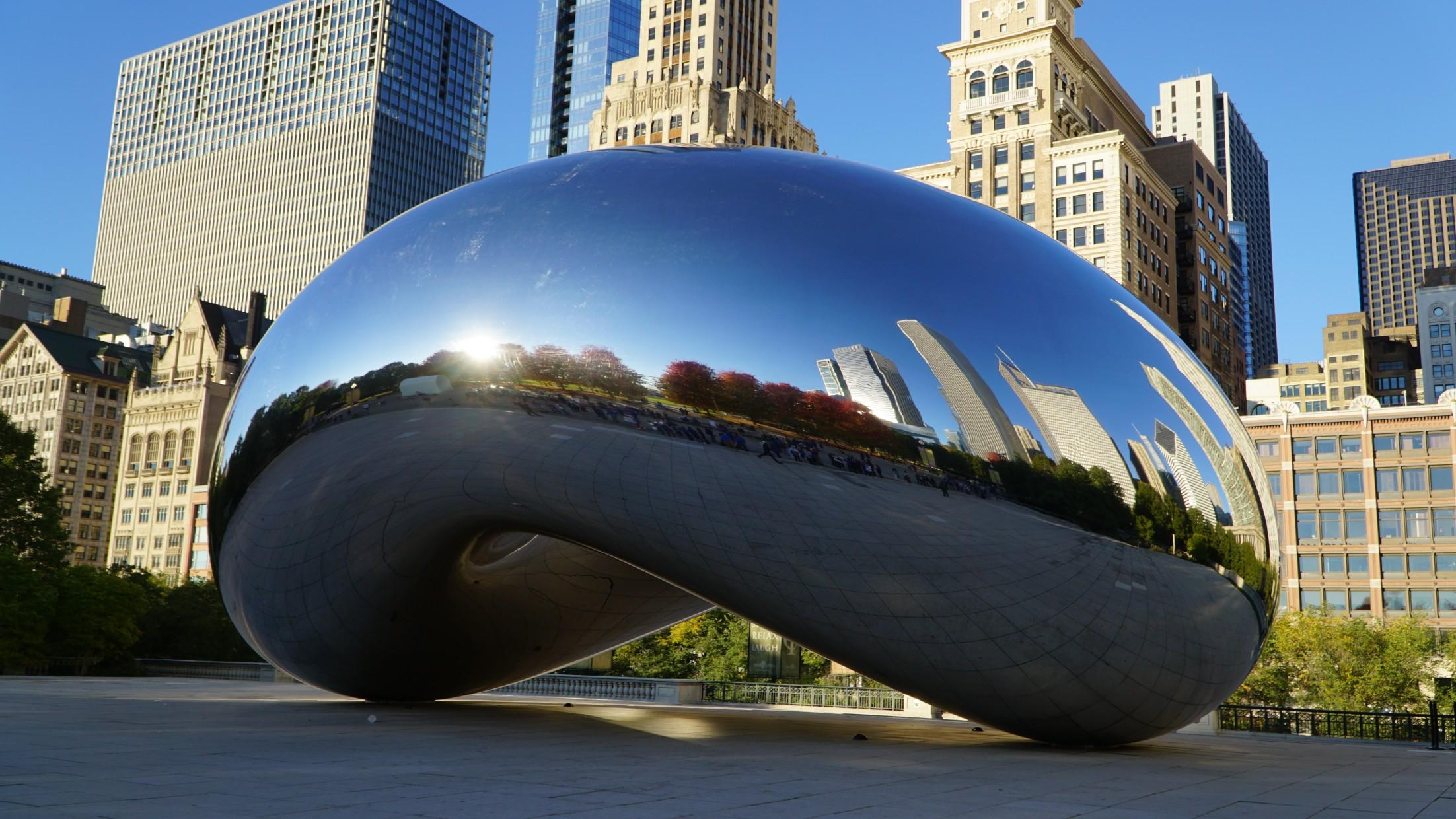 The Cloud Gate sculpture reflects Chicago buildings in Millennium Park on a sunny day.