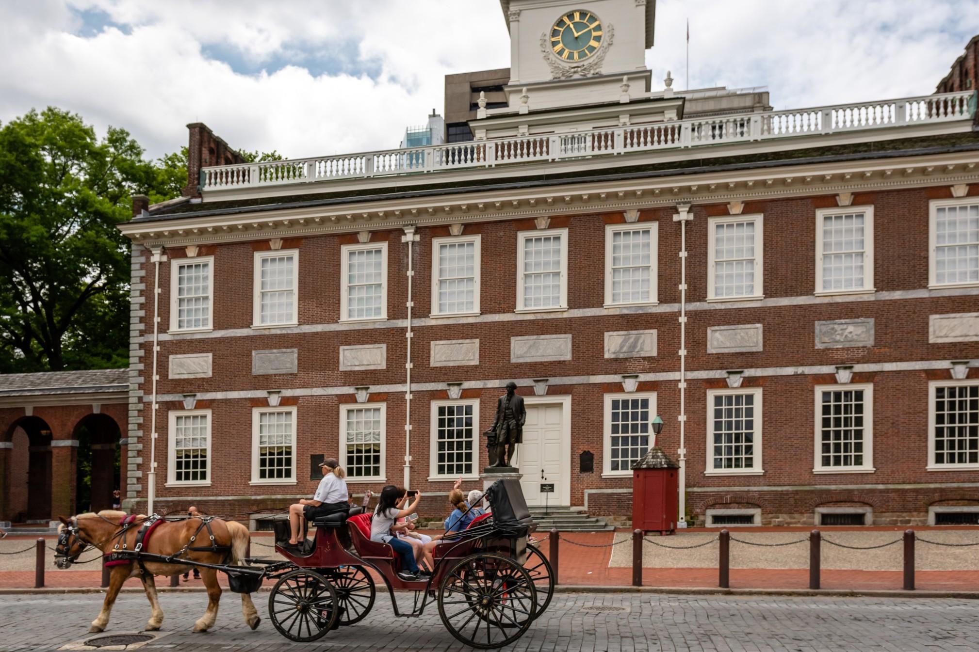 A horse-drawn carriage carries tourists past the brick facade of Independence Hall, Philadelphia.