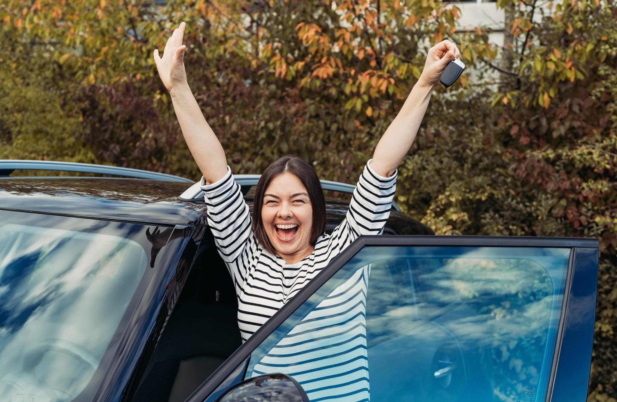 一个快乐的女人站在她的新车在得到她的驾照。