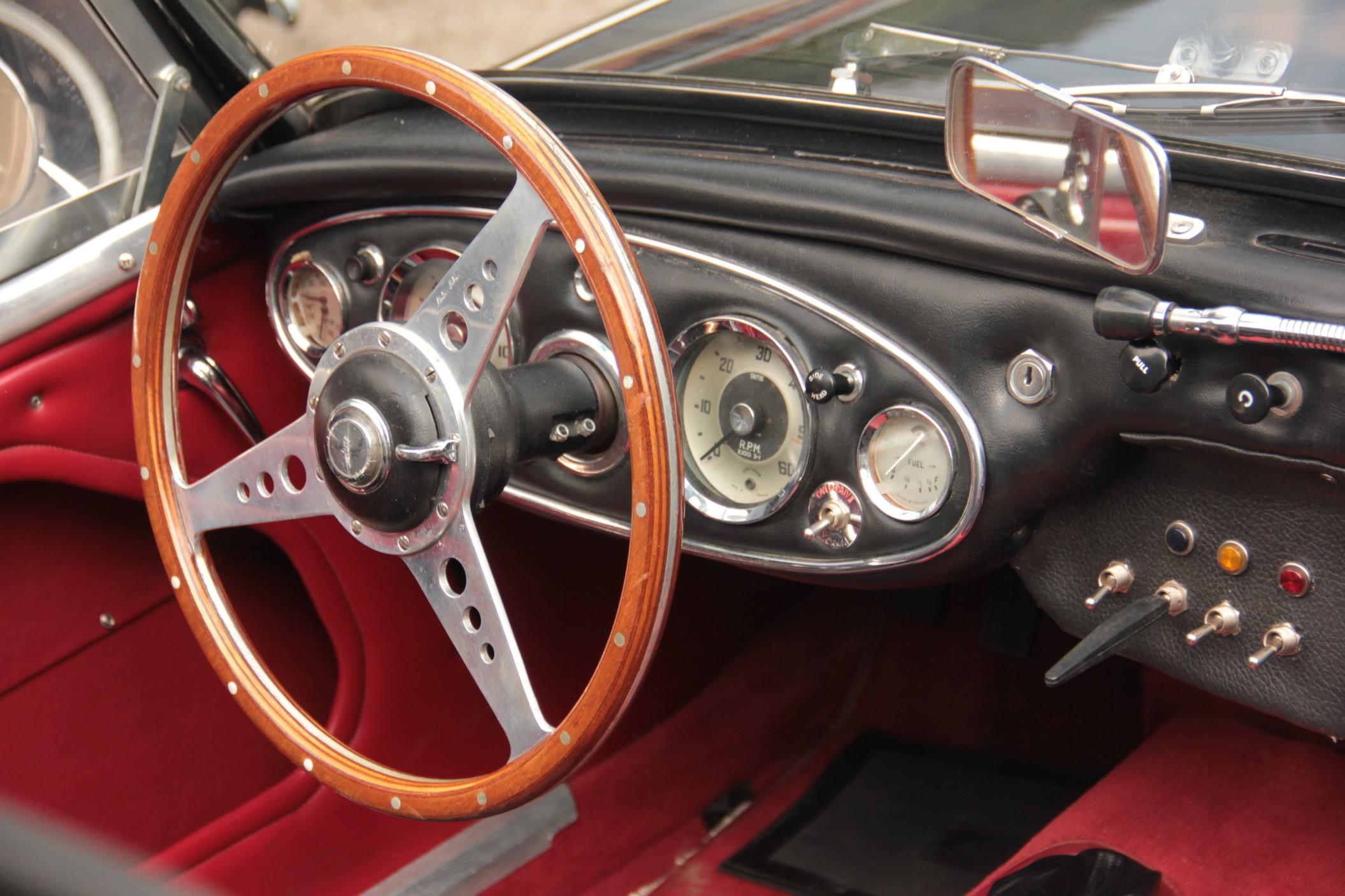 The thin brown steering wheel of a classic car with a red and black interior.