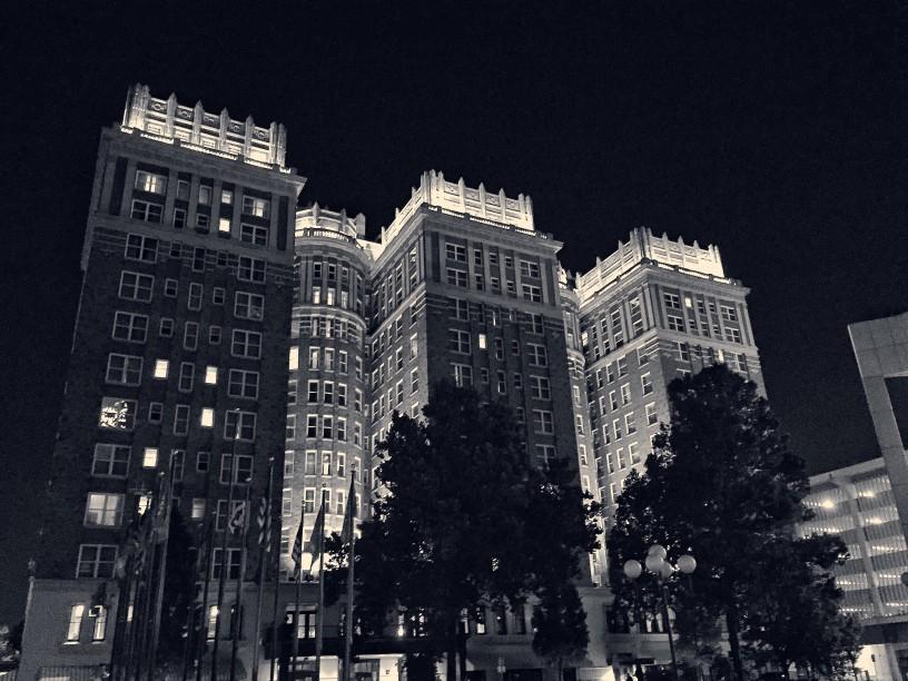 A black and white view looking up at the Skirvin Hotel illuminated at night.