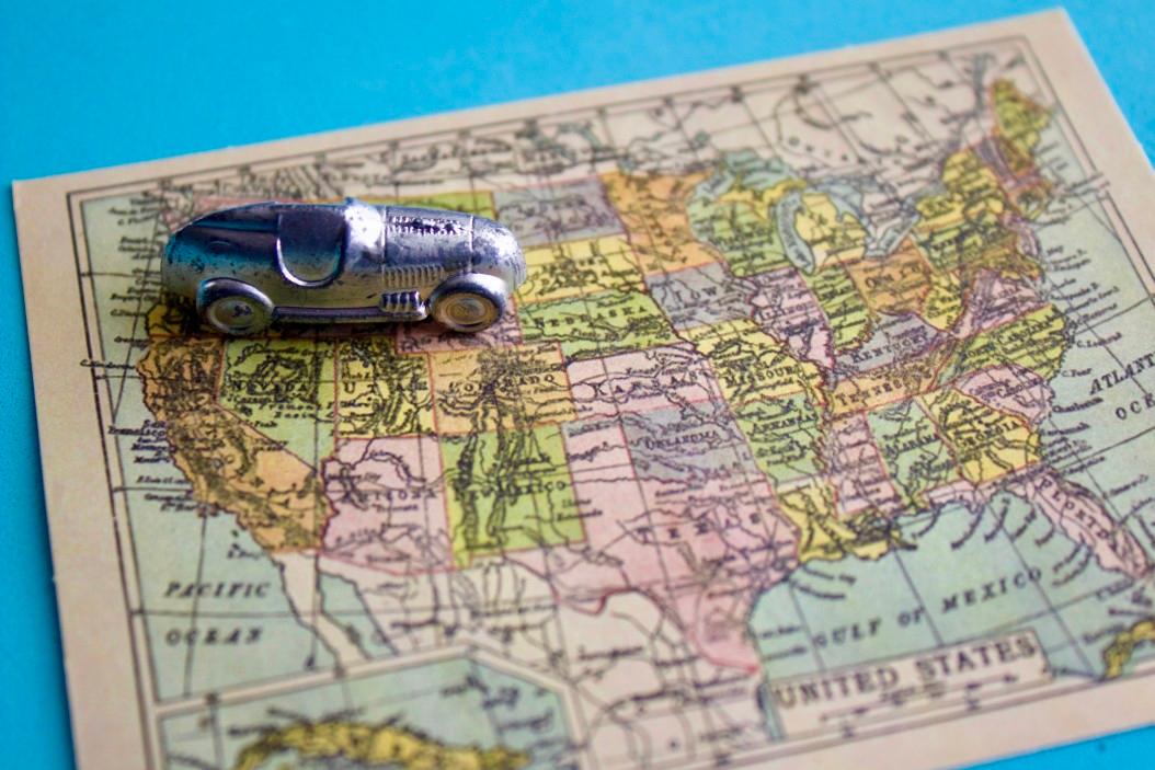 A miniature silver monopoly car game piece on top of a map of the United States
