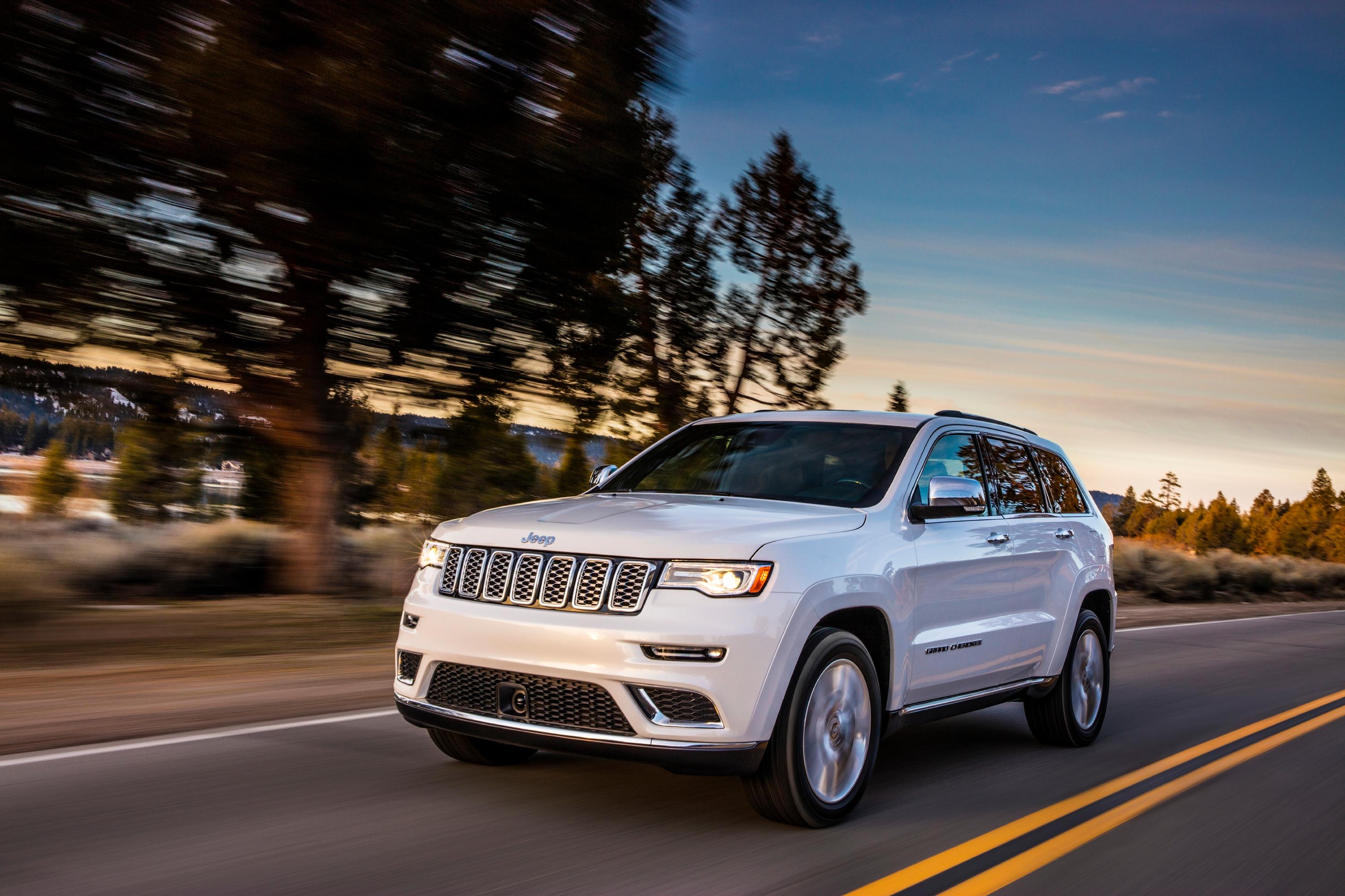 Image of a white Jeep Grand Cherokee driving at sunset. 