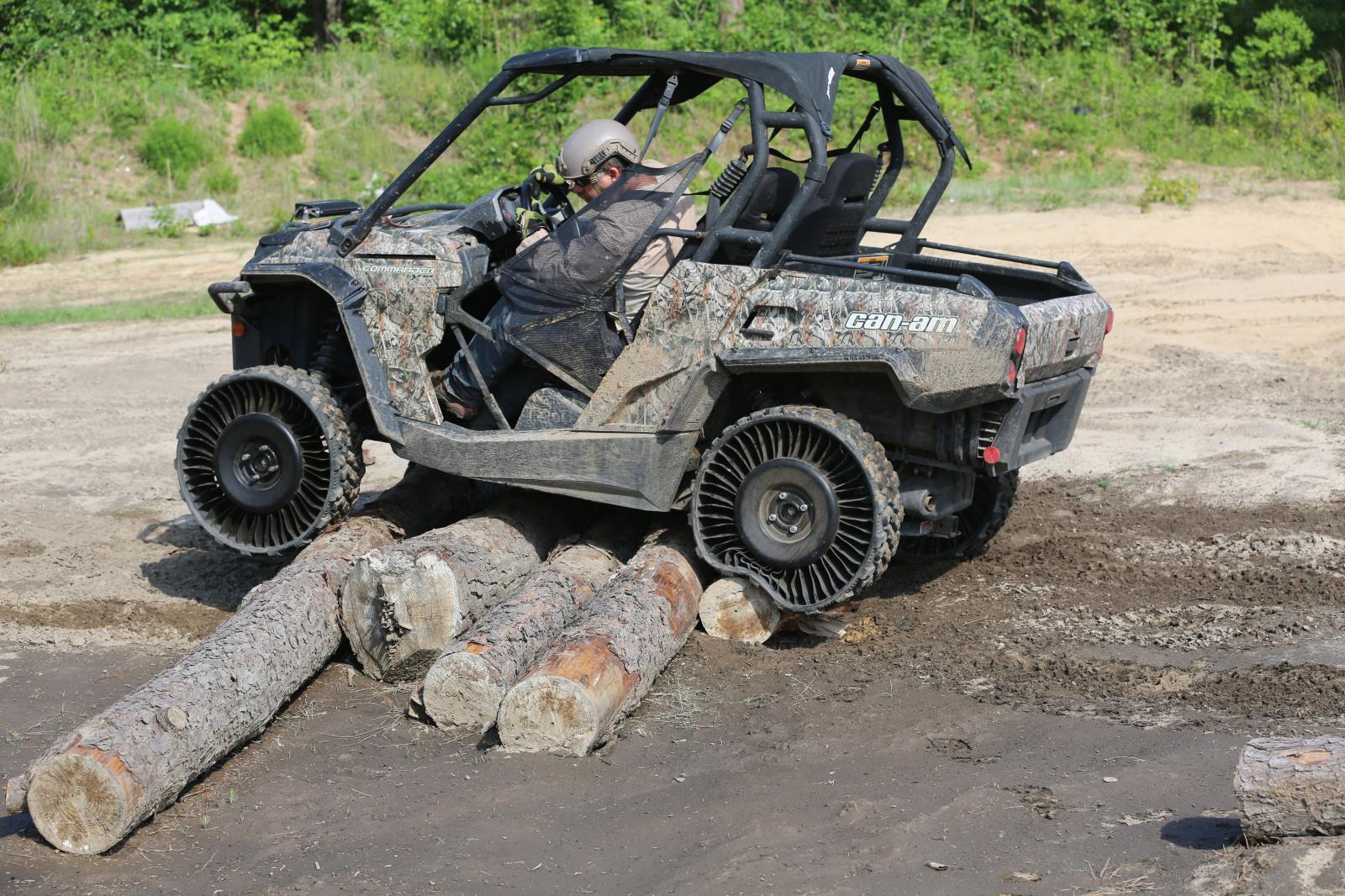 A UTV with airless tires climbing over a pile of logs.