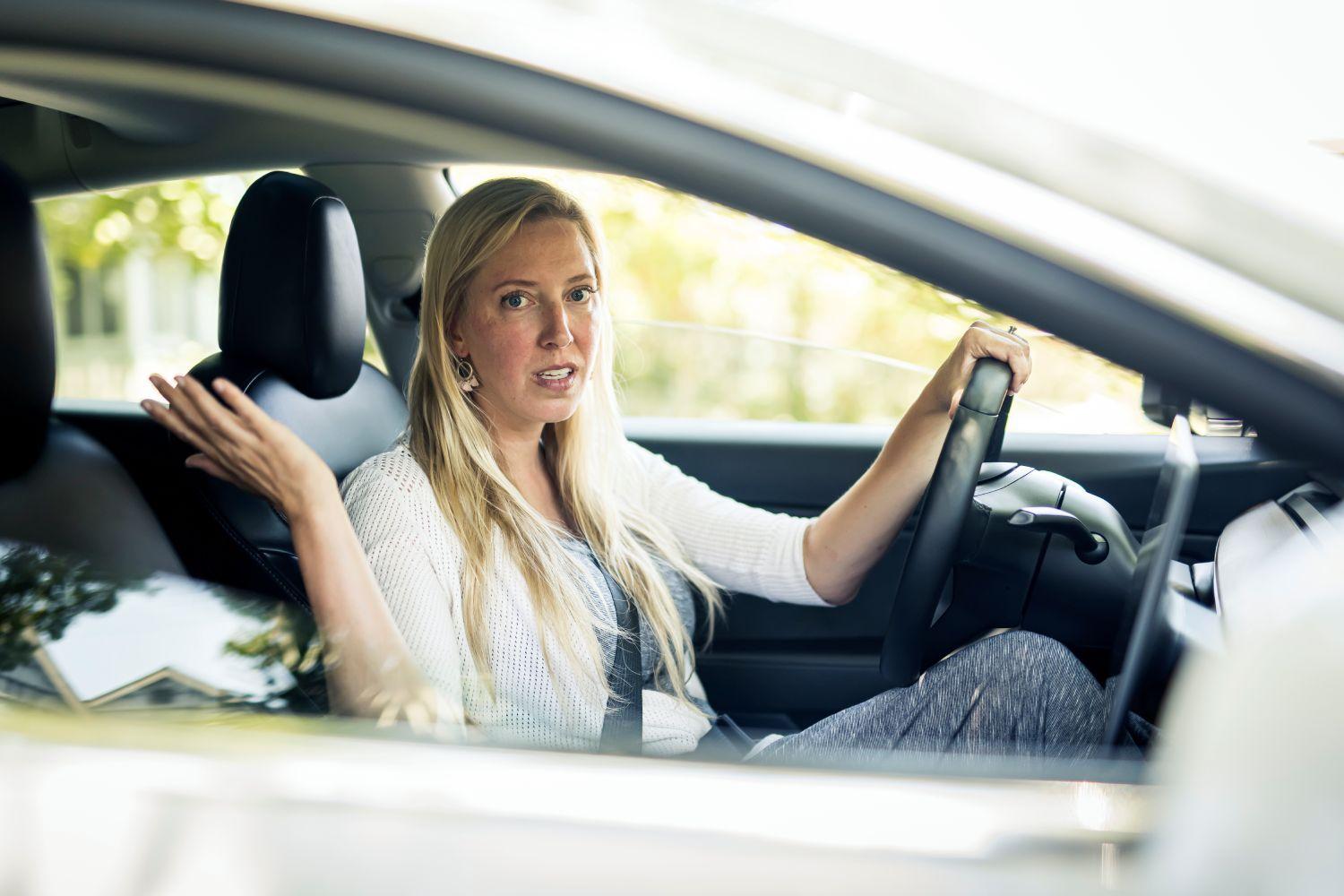 A woman looking frustrated while behind the wheel of her car.