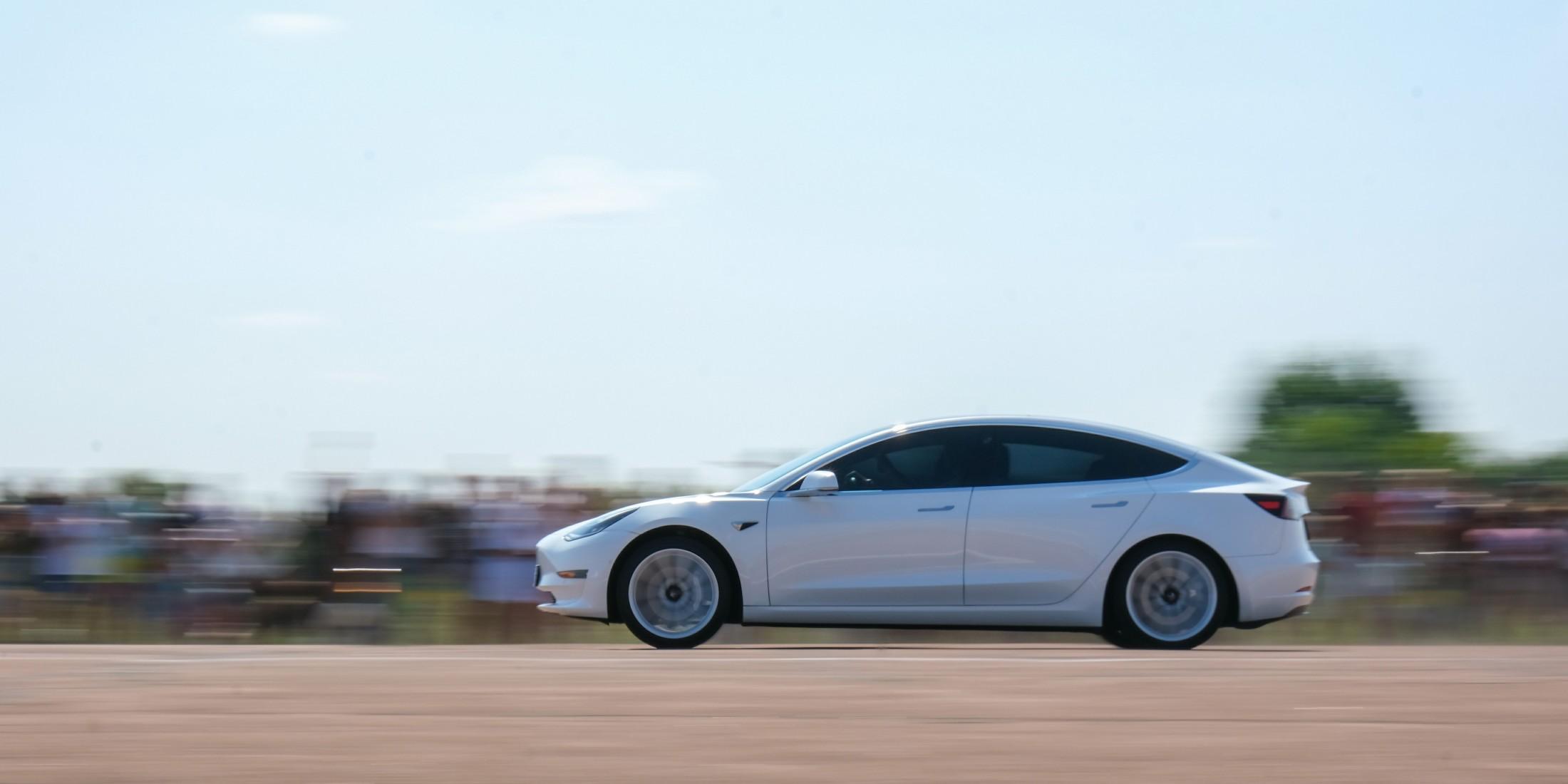 A side view of a white Tesla driving 