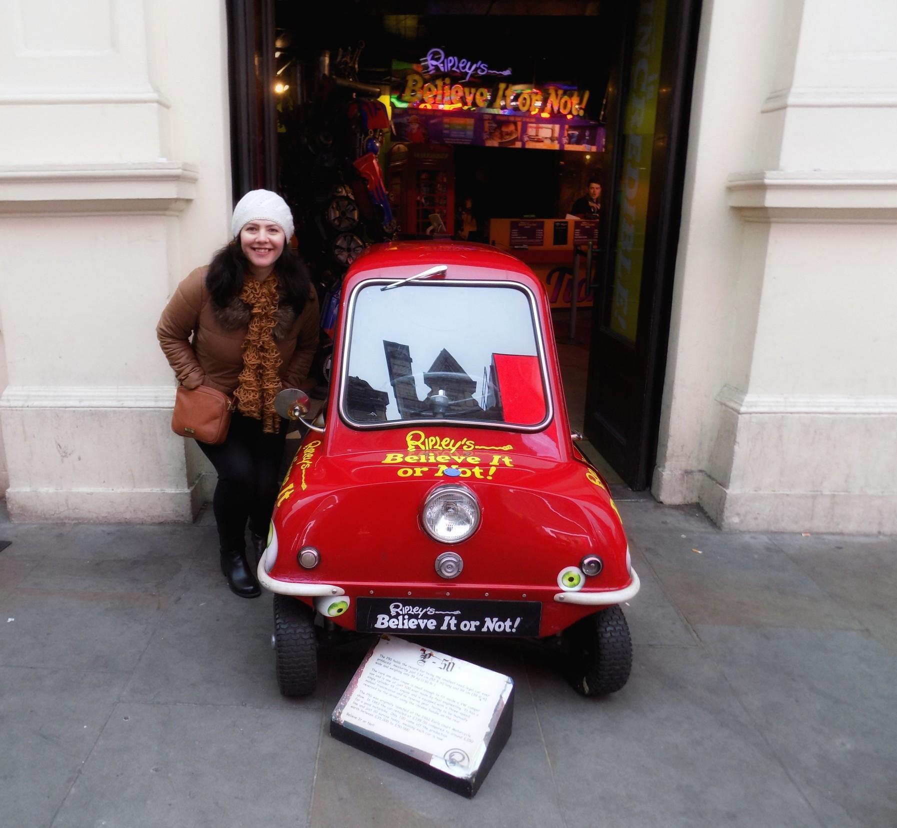 A woman standing next to the smallest car in the world.
