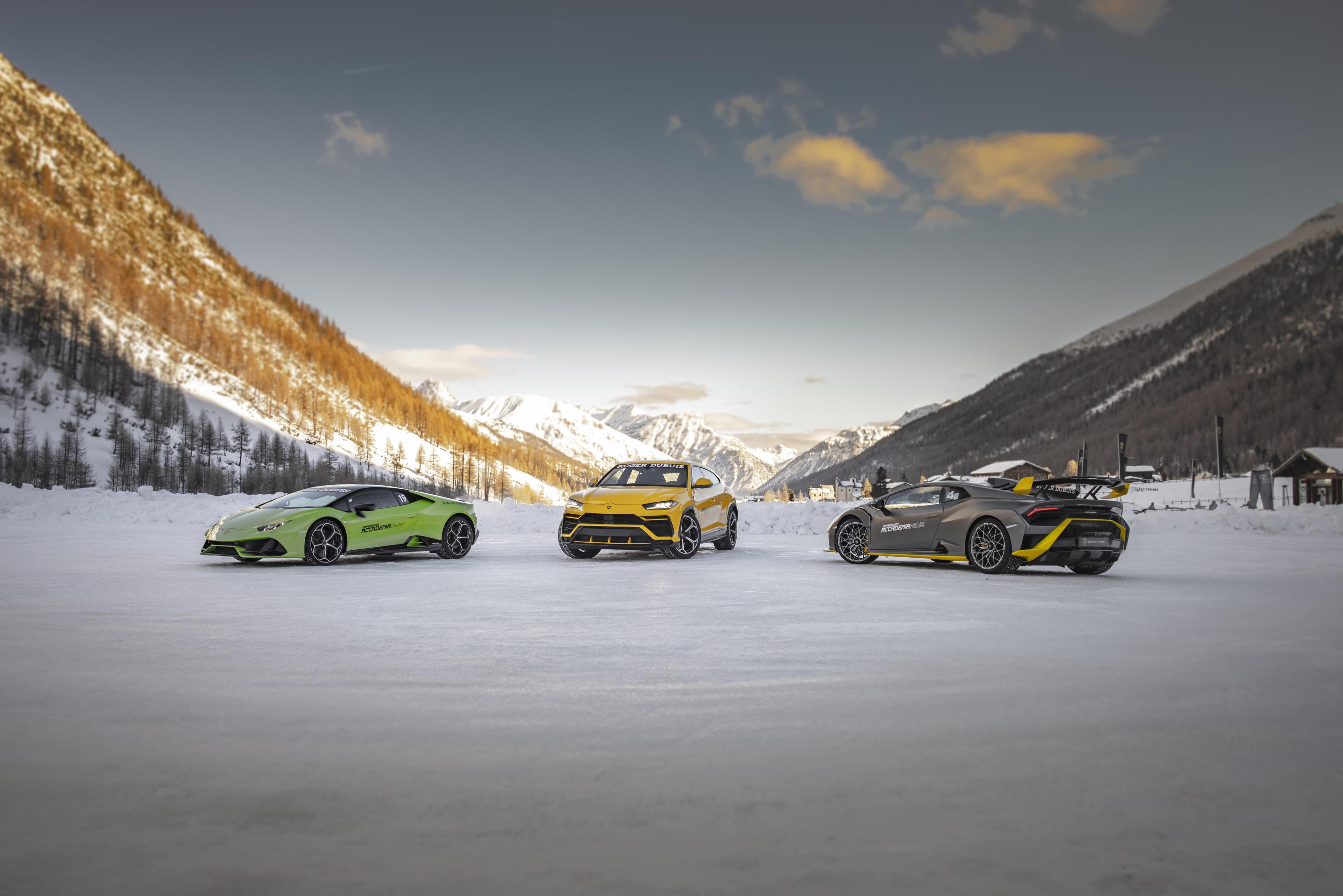A lineup of various Lamborghini cars against a snowy mountainous backdrop.
