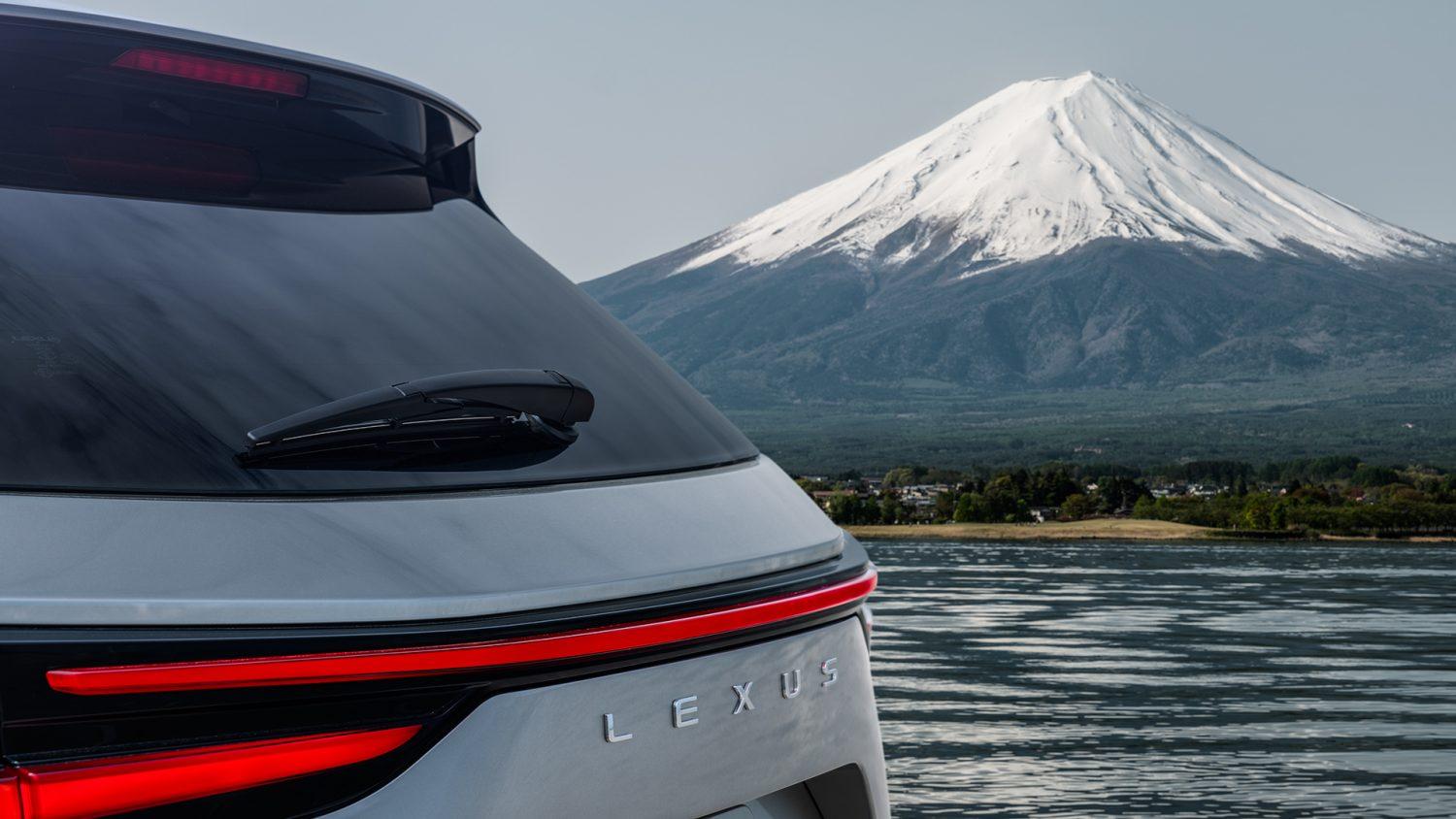 A view of the back of a gray Lexus NX with a mountain and a lake in the background.