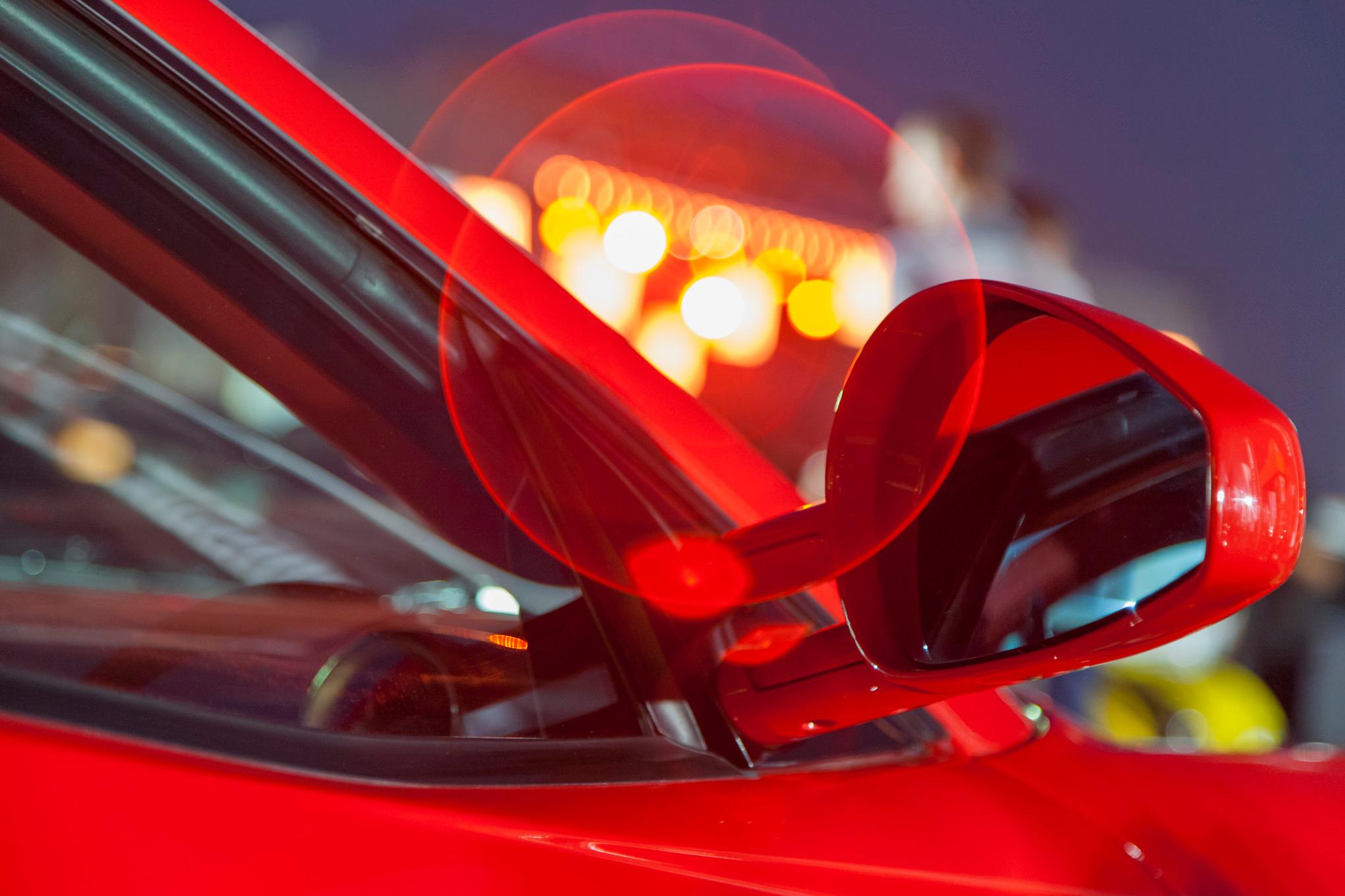 closeup of a the passenger-side window of a red car in front of city lights