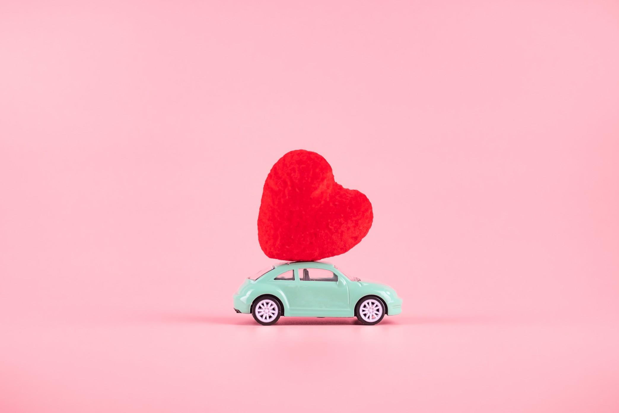 red heart on a teal car toy with a pink background