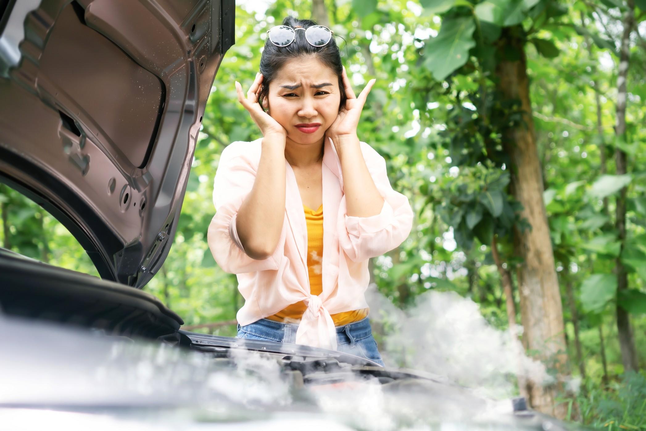 A woman looking at her car overheating.