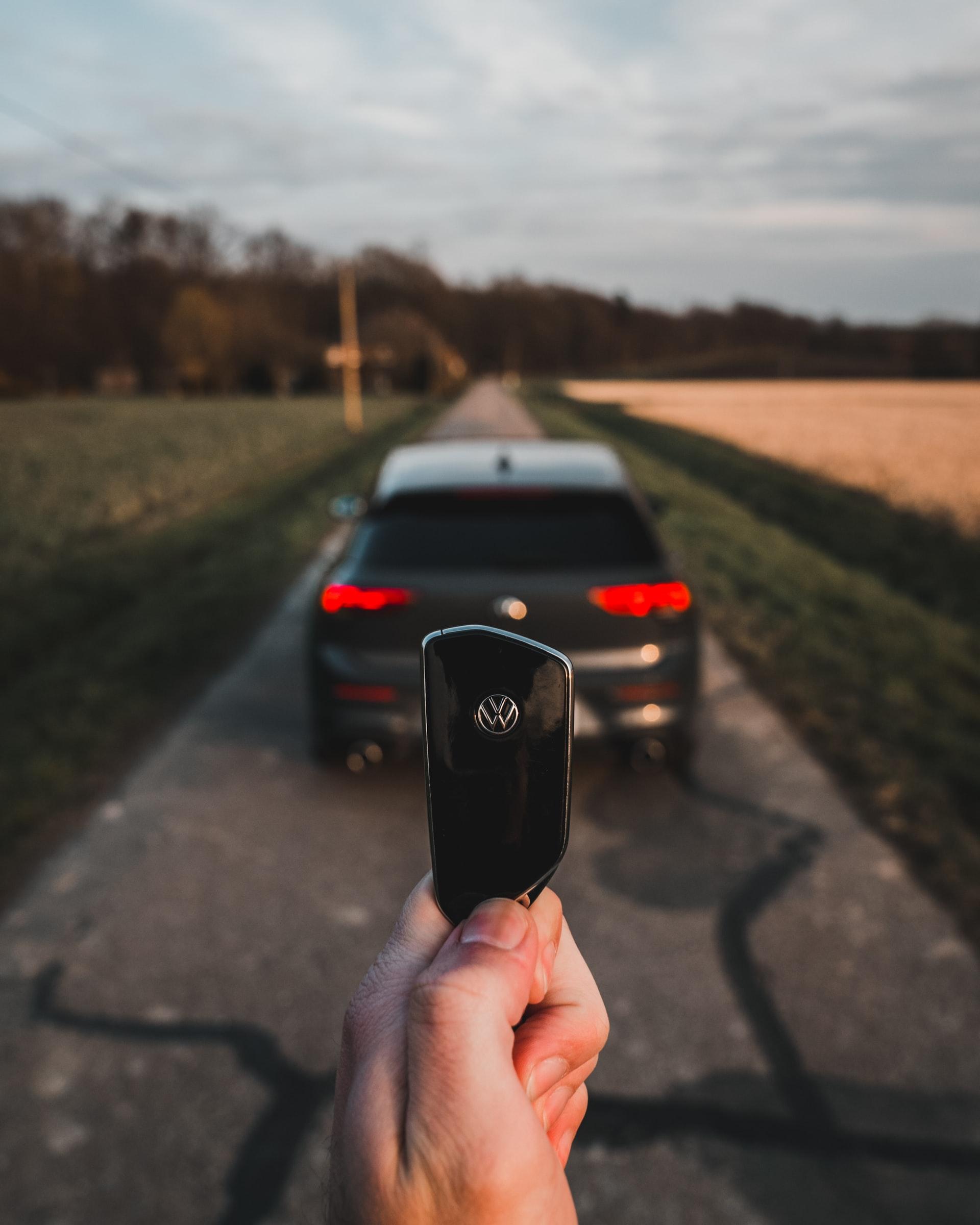 Hand holding a VW car key in front of a black VW sedan