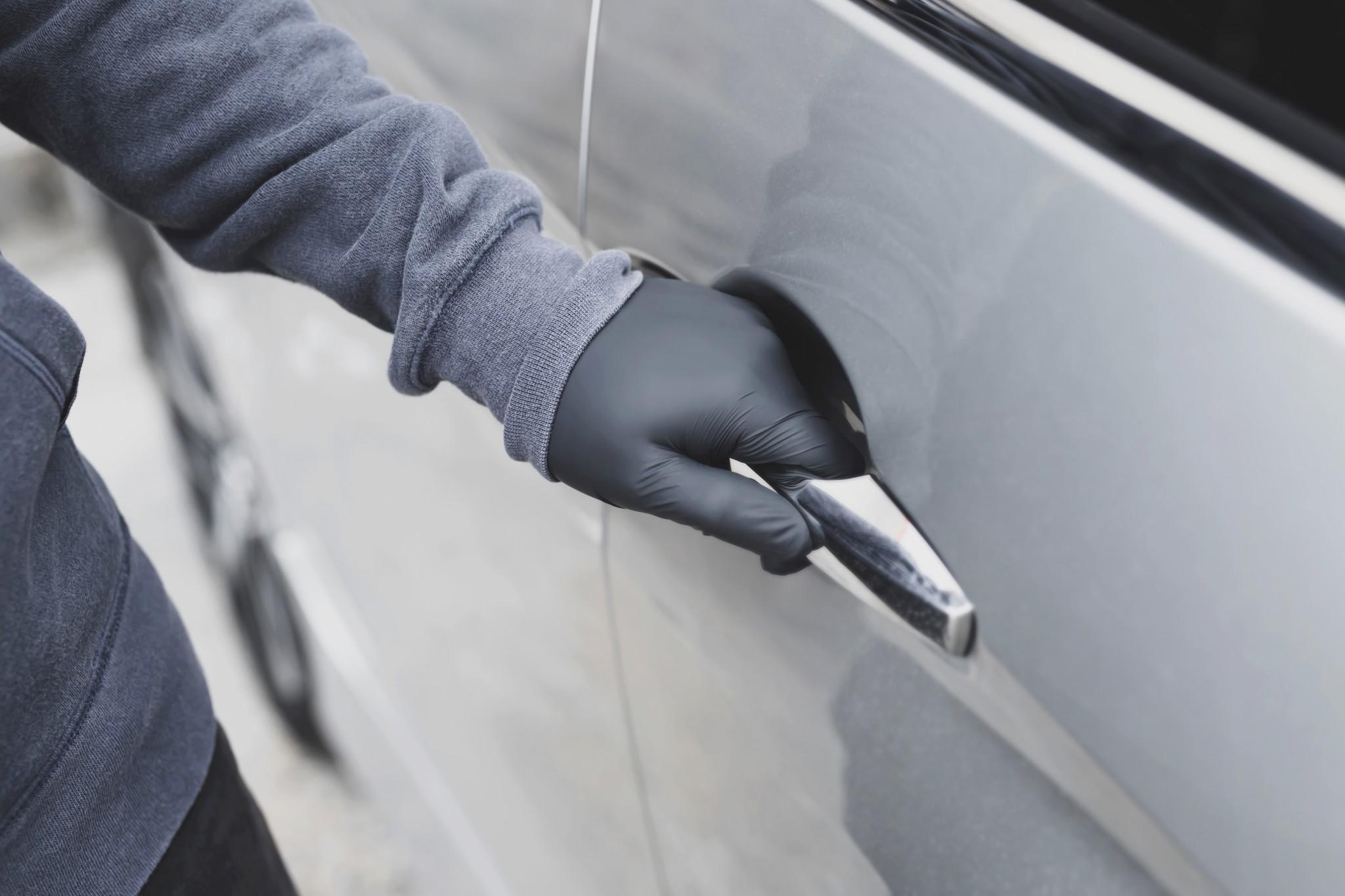 A gloved thief's hand on the door handle of a car
