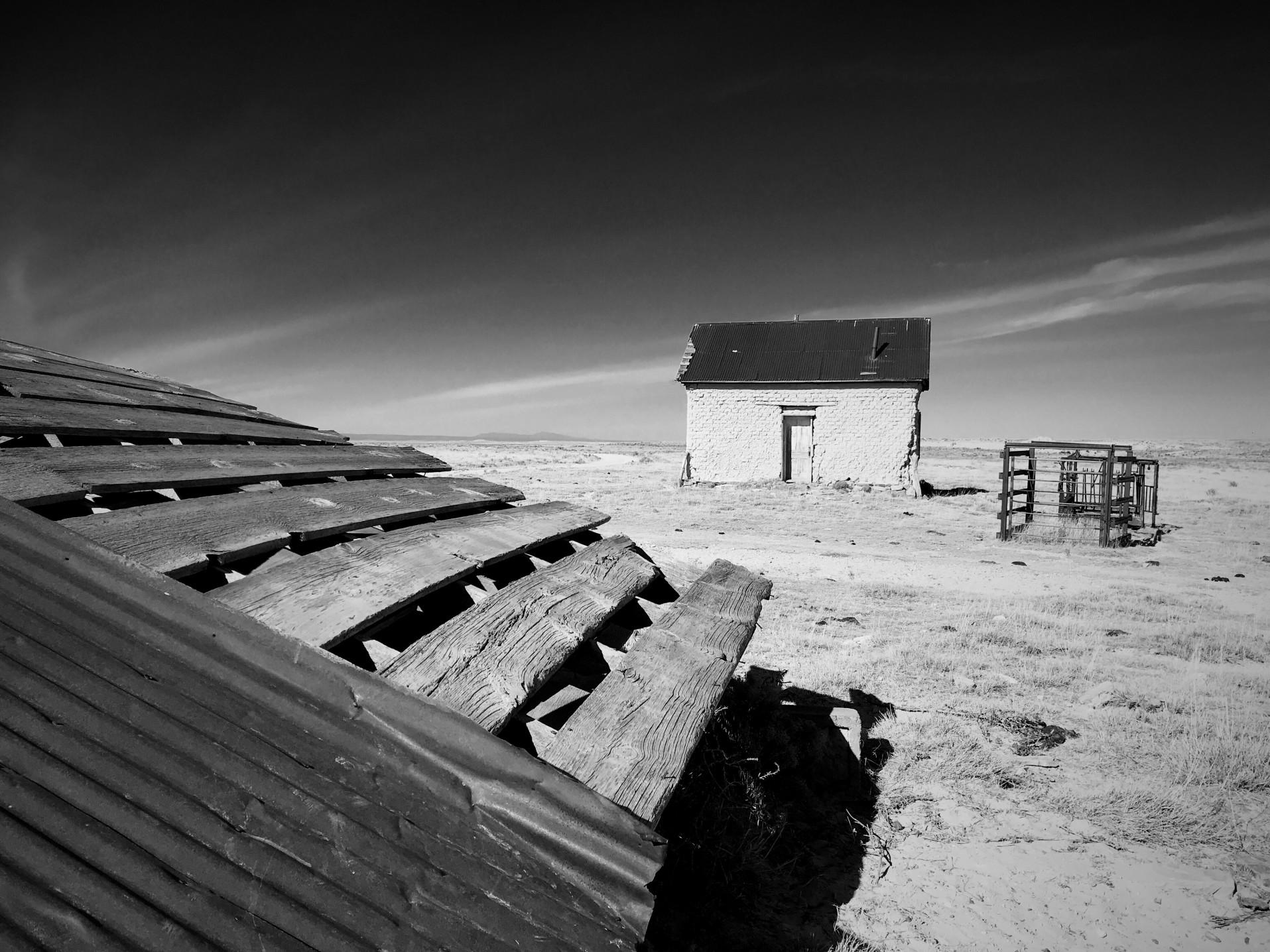 View of a small farm building and farm equipment in an empty desert.