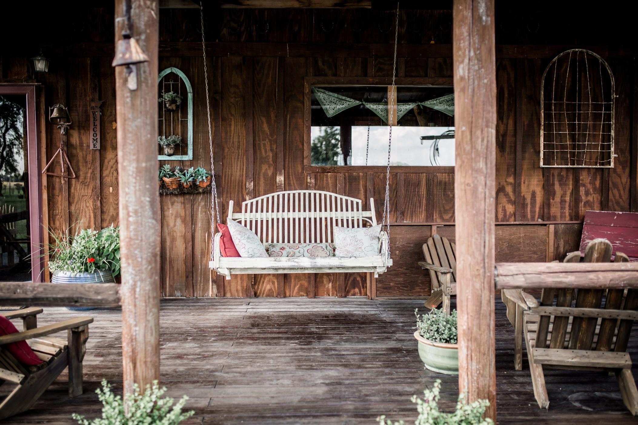 View of a rustic porch with seating, and a hanging porch swing surrounded by plants. 
