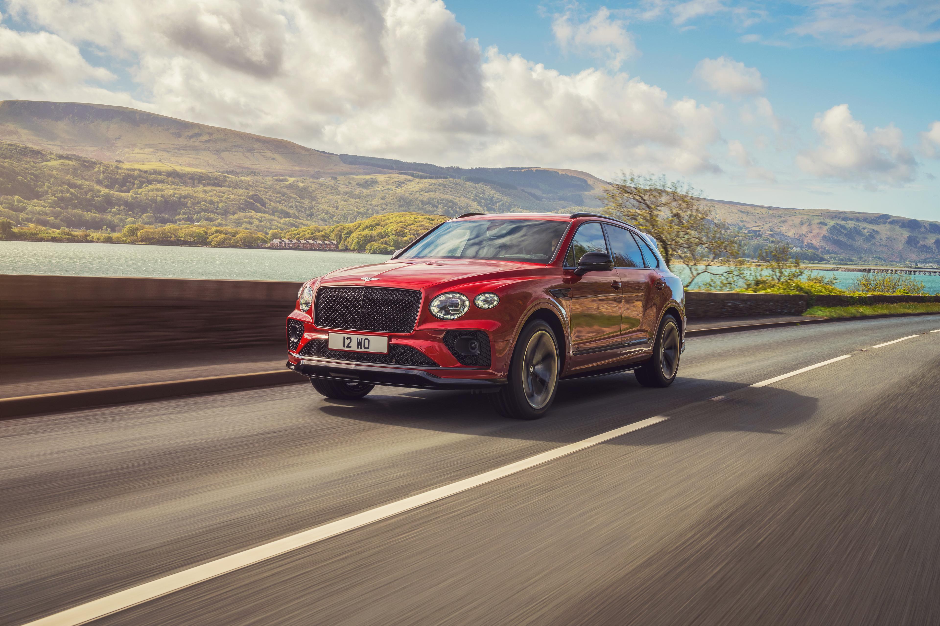 A red Bentayga S driving on an open road with a mountain in the background 