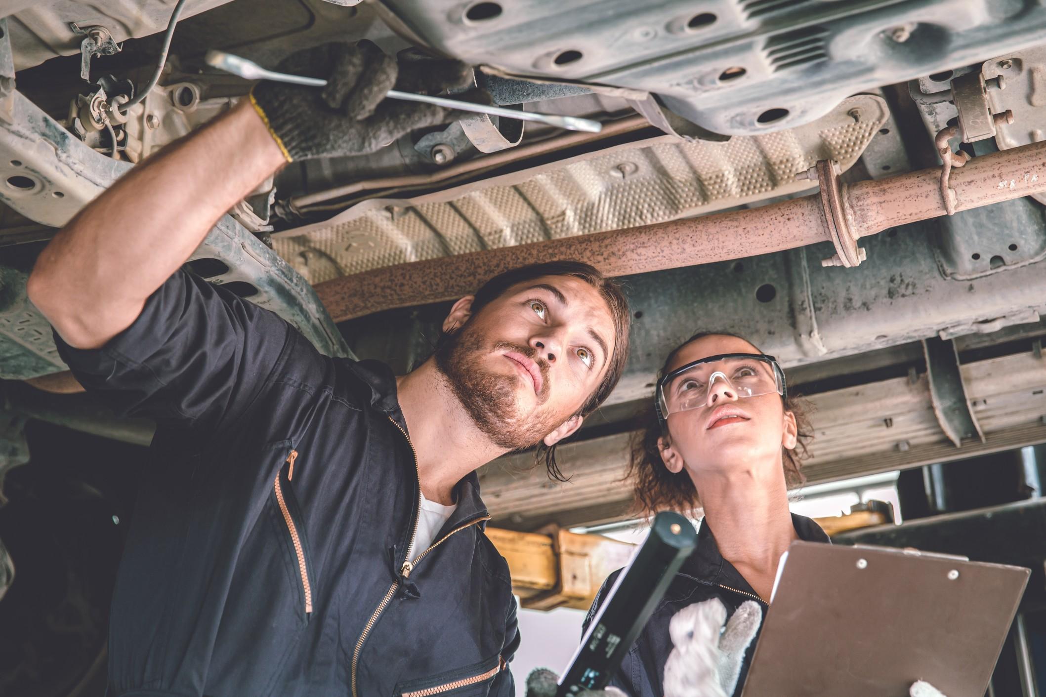 Man and woman looking at the underside of a car for maintenance
